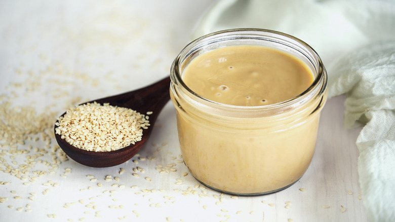A top view of a Mason jar with sesame paste inside, with a spoonful of sesame seeds next to it