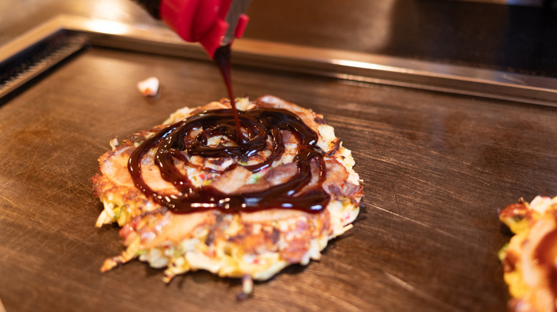 Okonomiyaki sauce is poured onto an okonomiyaki pancake