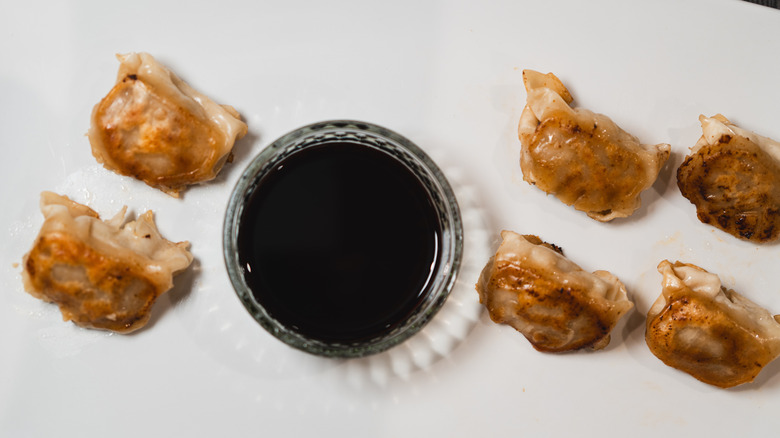 An overhead view of crispy pan-fried dumplings, served with a bowl of tare sauce