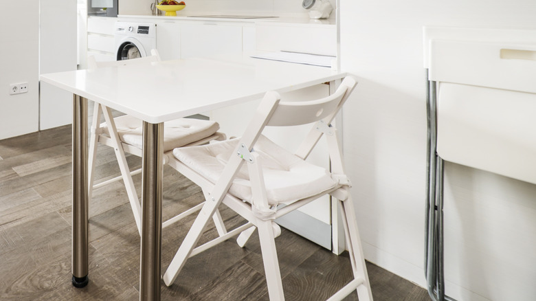 White, wooden folding chairs at a table and against a nearby wall