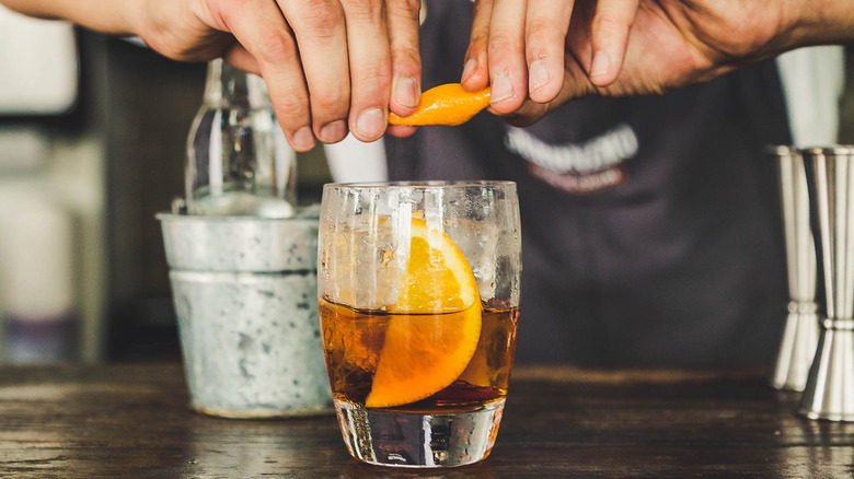 Hands squeezing orange into cocktail