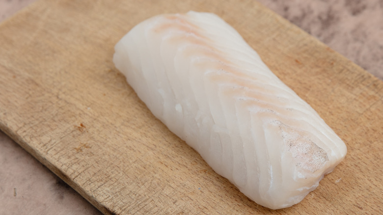 A fillet of cod on a wooden board.