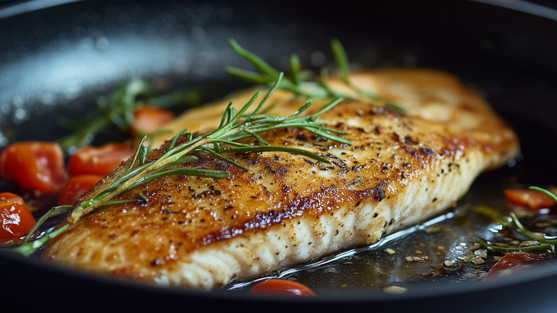 Seared white fish in a pan with rosemary and halved cherry tomatoes.