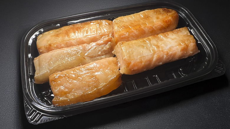 Five pieces of salmon belly arranged on a black takeout tray