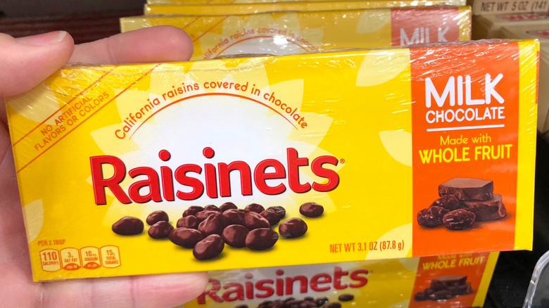 A hand holds a box of Raisinets, with more boxes in the background