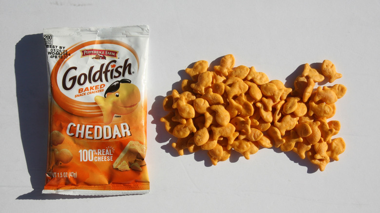 A package of Pepperidge Farm Goldfish Cheddar Snack Crackers are seen next to a pile of crackers, on a grey background