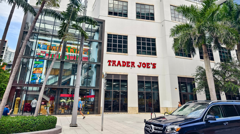A Trader Joe's as part of a building on a city block, with palm trees and a Mercedes parked in front.