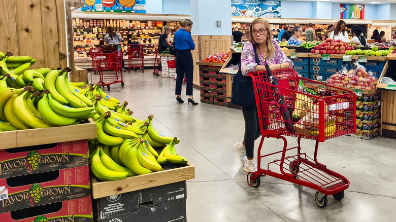 A woman shopping at Trader Joe's looks forlornly at bananas.