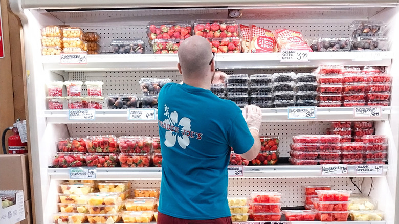 A Trader Joe's employee restocks berries in an open refrigerator.