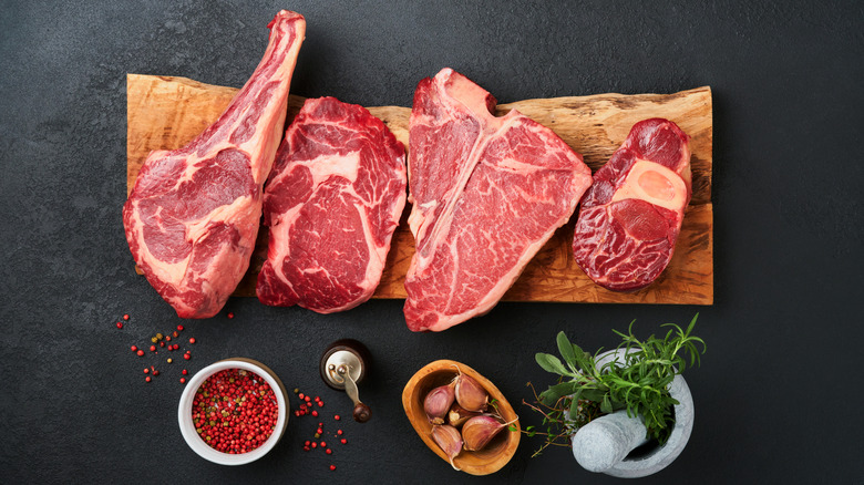 Several raw steaks on a wooden cutting board with spices and herbs