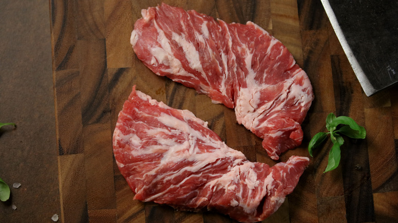Two oyster steaks on a wooden cutting board next to a cleaver