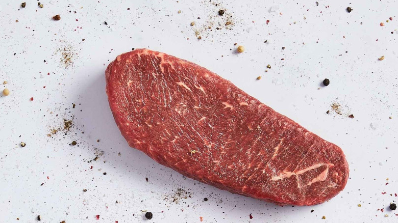 A ranch steak on a white surface with sprinkles of seasoning