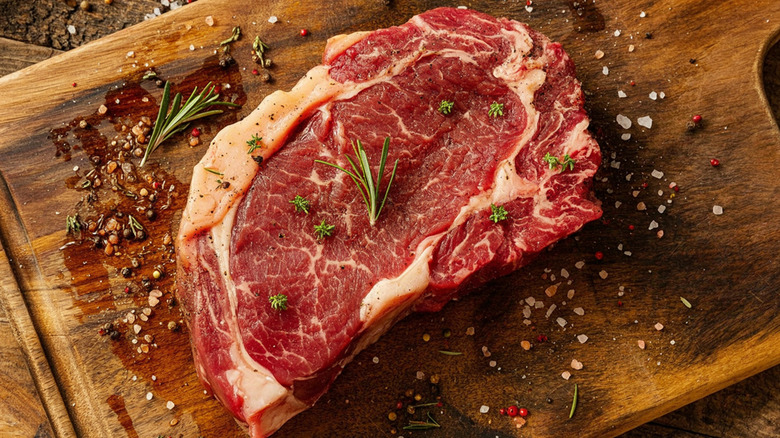 A raw ribeye seasoned on a wooden cutting board