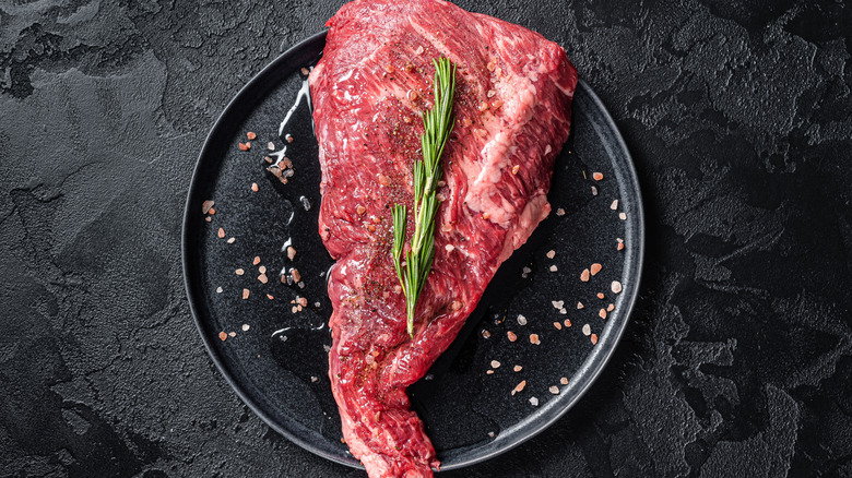 A raw tri-tip steak seasoned and garnished with a sprig of rosemary