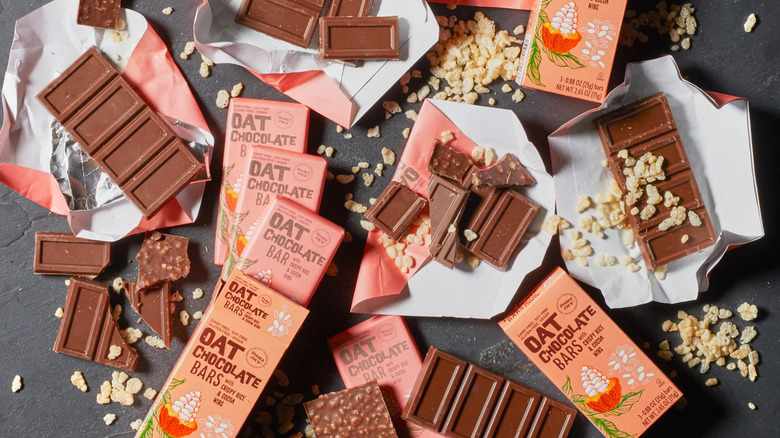 Pieces of crispy rice and cocoa nib oat bars with oats on wrapping with whole pink and peach bars on the table.