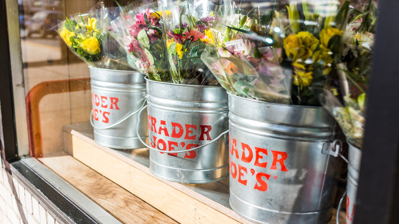 Metal buckets of assorted plastic-wrapped bouquets of flowers at Trader Joe's with the store logo on them