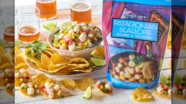 A bag of Trader Joe's Patagonian Scallops with some of them in ceviche and on chips on a white painted wooden table with beers in the background.