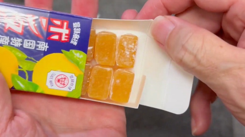 A hand removes sleeve of Bontan Ame orange candy pieces from its package