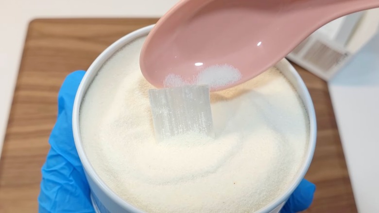 Plastic spoon scoops into container of shimobashira, white powder candy with transparent cady squares inside