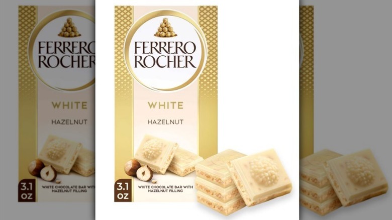 Ferrero Rocher white hazelnut bar in a gold package with pieces of white chocolate in front on white background