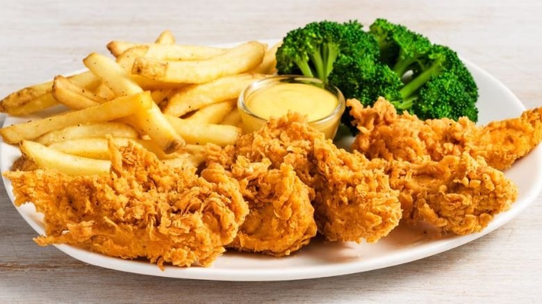 A plate of chicken tenders, fries, and broccoli on a plate.