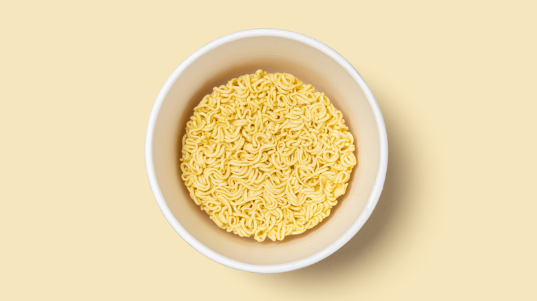 Bowl of dry, uncooked instant noodles, on a yellow background