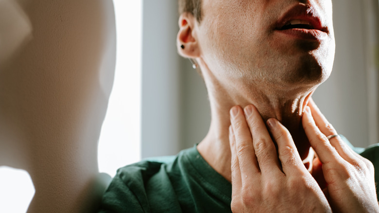 Man in green t-shirt holds his throat as if in pain