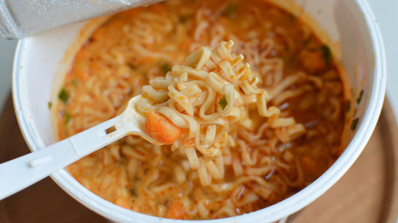 Instant cup noodles, with plastic fork scooping up noodles and vegetables