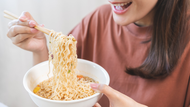 Person smiling while using chopsticks to pick up noodles from a bowl
