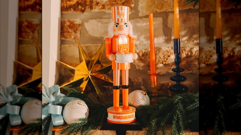 A nutcracker in orange and white stripes, holding a white cake with orange "75" candles on top