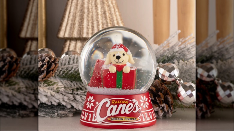 Raising Cane's Santa Cane Snow Globe, with a small yellow dog peeking out of wrapped presents