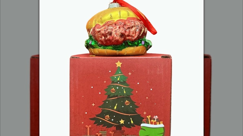A glass ornament of a hot chicken sandwich atop a Christmasy cardboard box