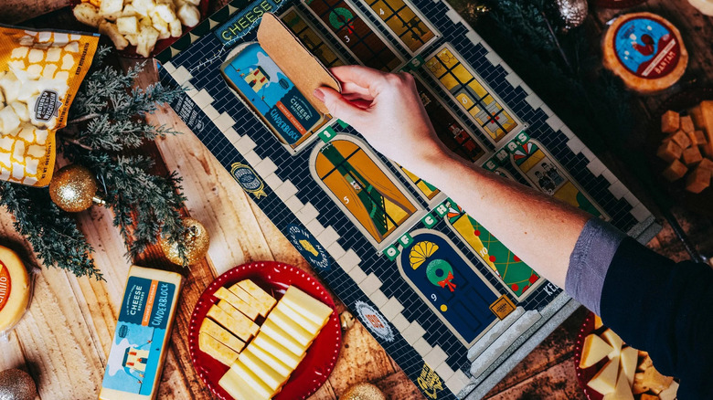 Hand opening advent calendar window to reveal cheese block