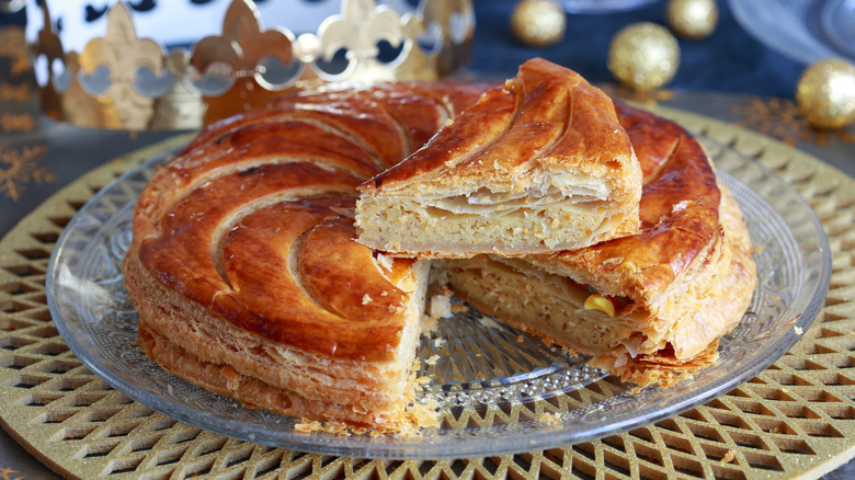 A galette de rois with a slice out of it balanced on top
