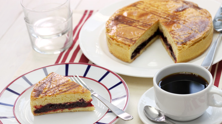 A gâteau Basque with a slice out of it on a plate next to a cup of coffee