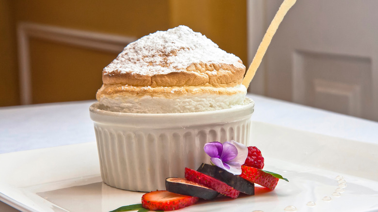 A fluffy soufflé garnished with powdered sugar and slices of fruit next to the ramekin