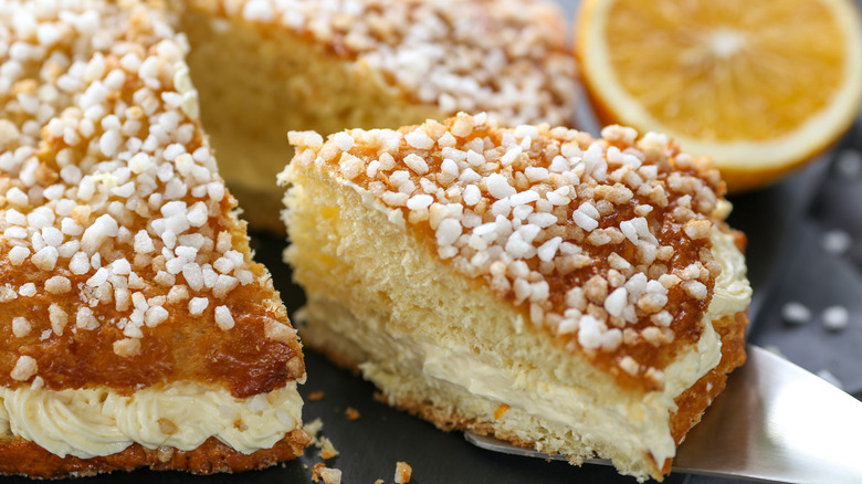 A tarte tropézienne with a slice being pulled out of it and a lemon half in the background