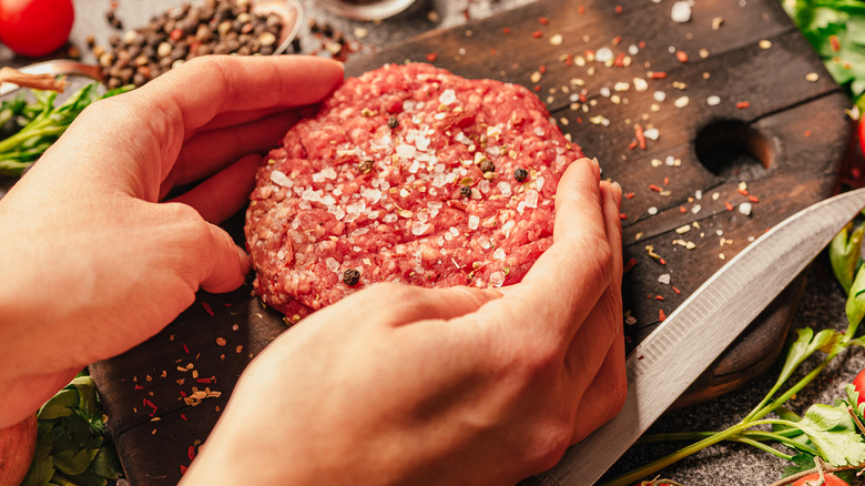 person seasoning hamburger patties