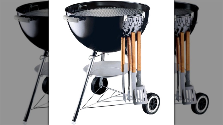 Grilling utensils hanging on a Weber charcoal grill tool holder on the side of a grill