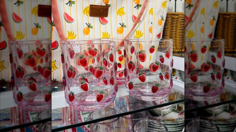 Strawberry-embossed tumblers on a shelf in front of a bag decorated with bananas, pineapple, and watermelon