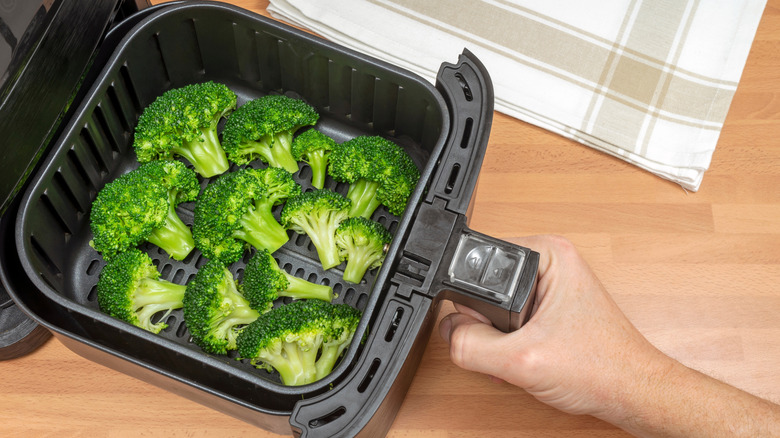 Broccoli florets being placed into air fryer