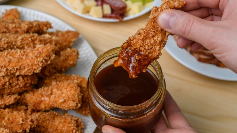 Chicken tender being dipped into BBQ sauce