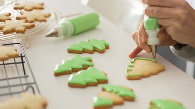 Person decorating green tree cookies with tipped piping bag