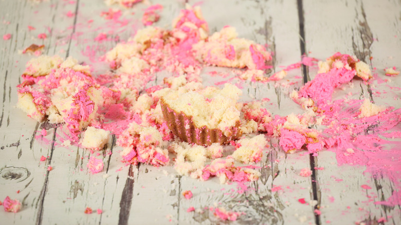 Pink icing and crumbled cupcake on a wood counter