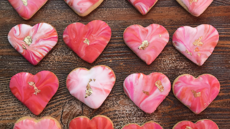 Pink, red, and white marbled heart cookies on a wood surface
