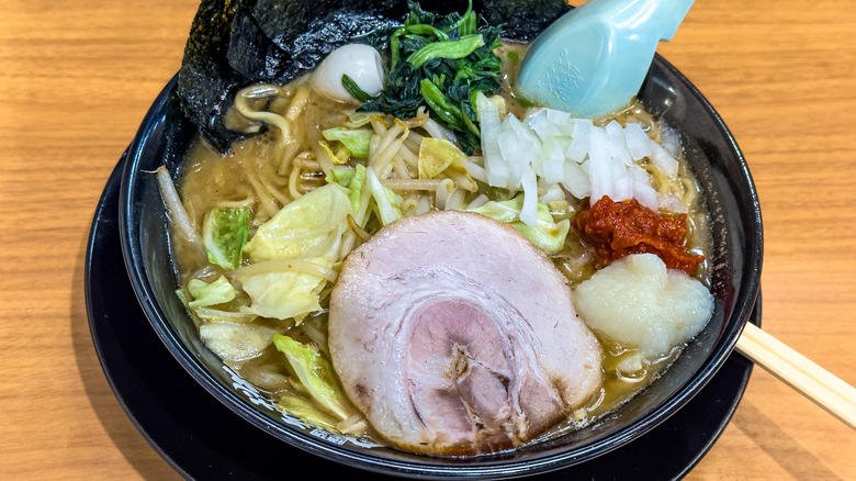 Bowl of miso ramen with abundant toppings, including a pork slice, sliced onions, cabbage, sautéed spinach, and nori sheets