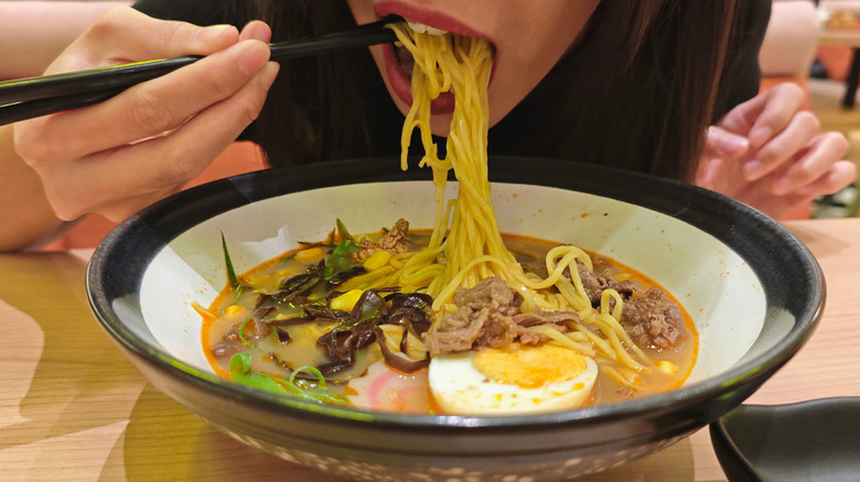 Close-up of a woman eating the noodles from a bowl of ramen