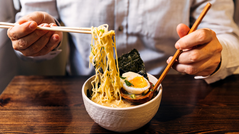 Person scooping noodles out of a ramen bowl with chopsticks