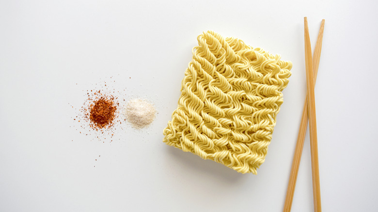 Nest of uncooked instant ramen, with two small piles of powdered seasoning and a pair of chopsticks next to it
