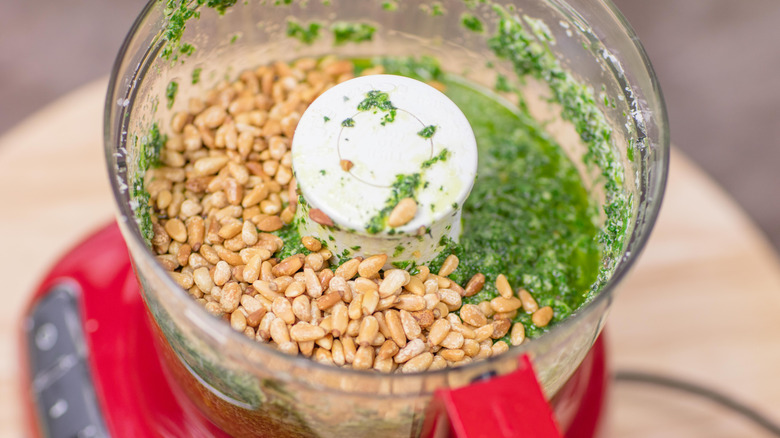 toasted pine nuts in food processor with blended ingredients that make pesto